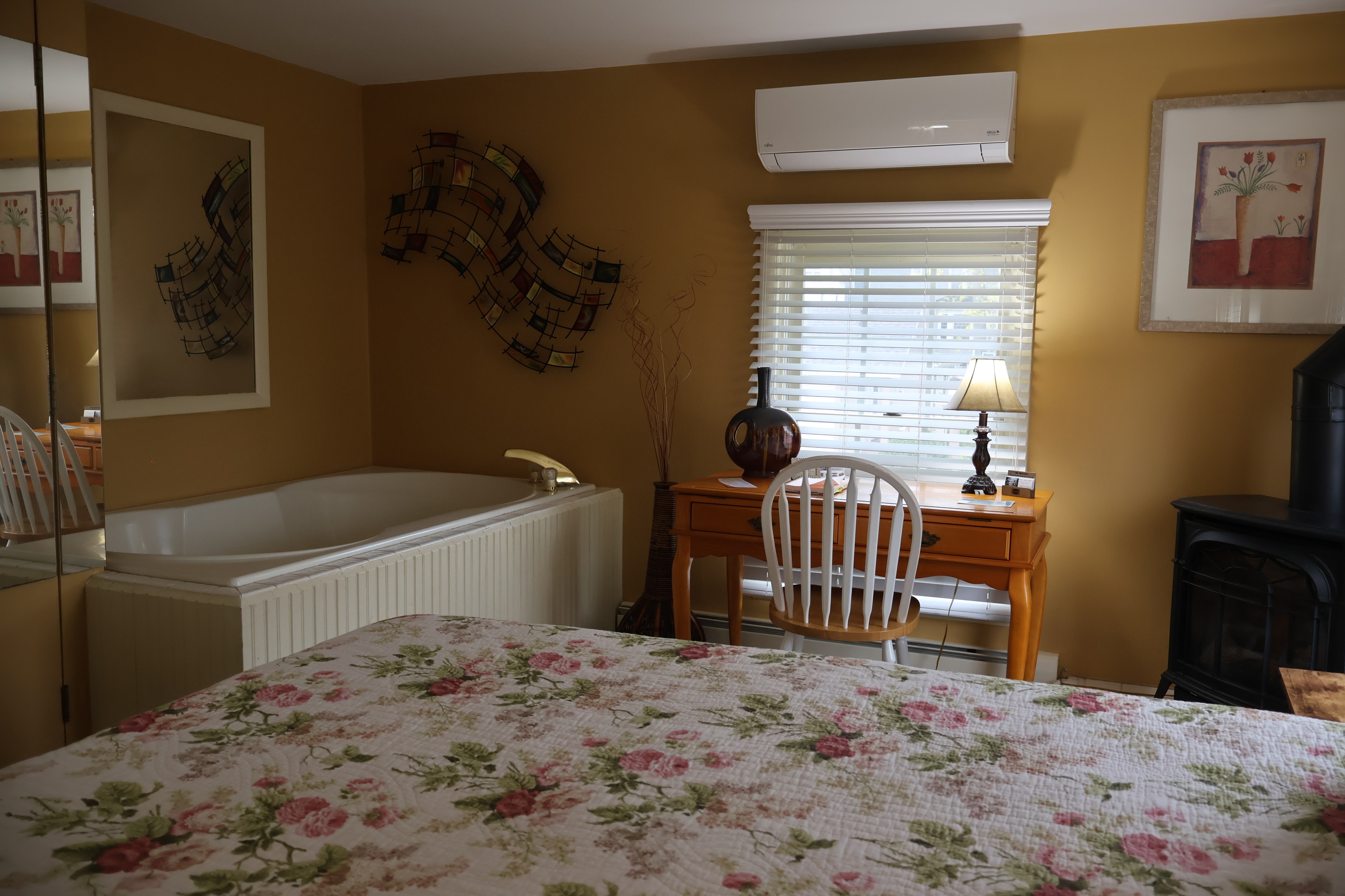 Bedroom with floral-quilted bed, a jetted tub, a desk, and a wall-mounted air conditioner.