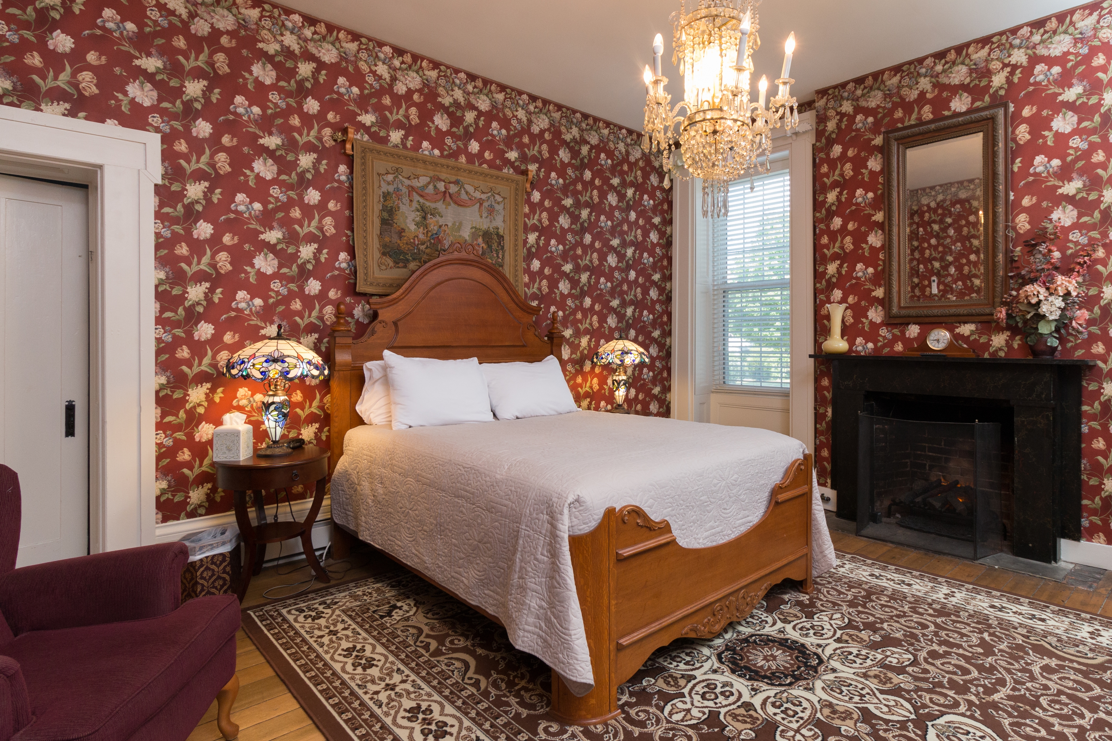 Mansion bed with tan quilt in bedroom with chandelier and fireplace