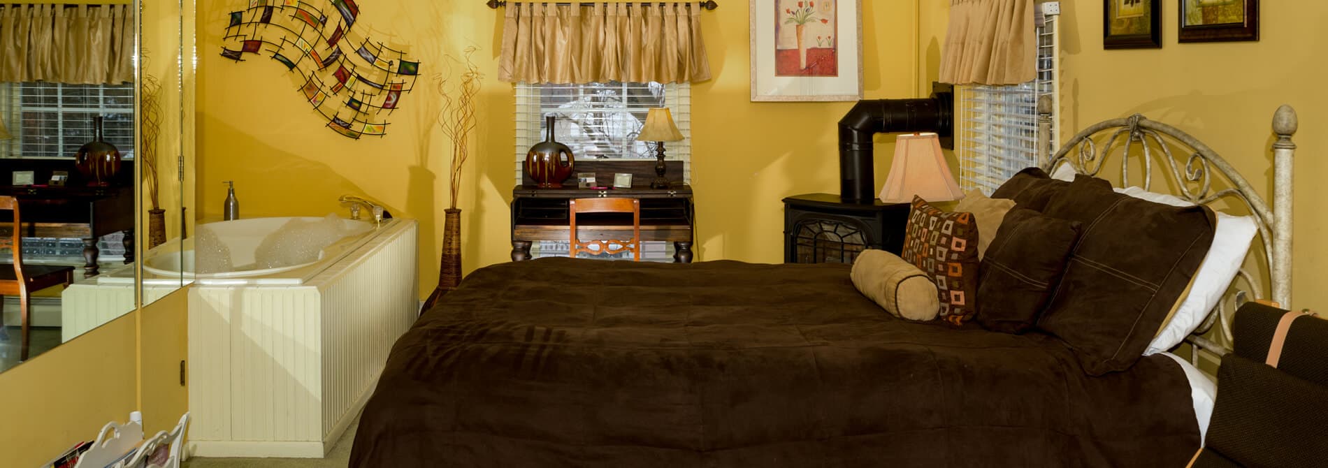 Bedroom with queen bed topped with dark brown quilt. The walls are painted a rich yellow with modern artwork.