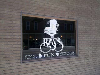 Signage for Ray's, featuring the words "Food, Fun, Spirits" alongside a graphic of a beer mug and a plate with food, displayed in a window.