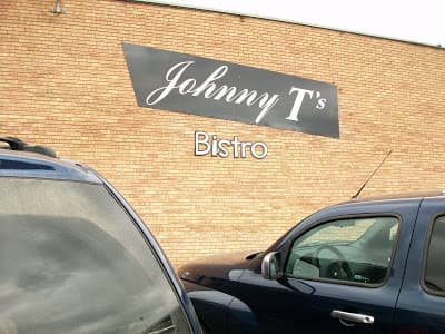 Sign for "Johnny T's Bistro" on a brick wall, with parked cars in the foreground.