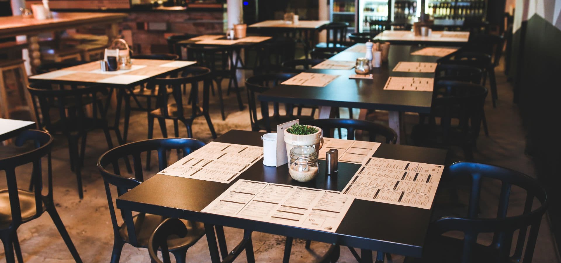A modern restaurant interior with black tables, empty chairs, and menus displayed on each table.