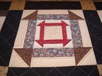 A colorful quilt block featuring a central square surrounded by patterned strips and triangular corners.