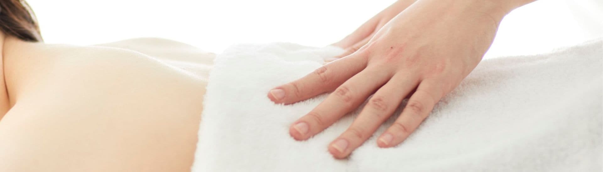 A hand resting gently on a back covered with a white towel.