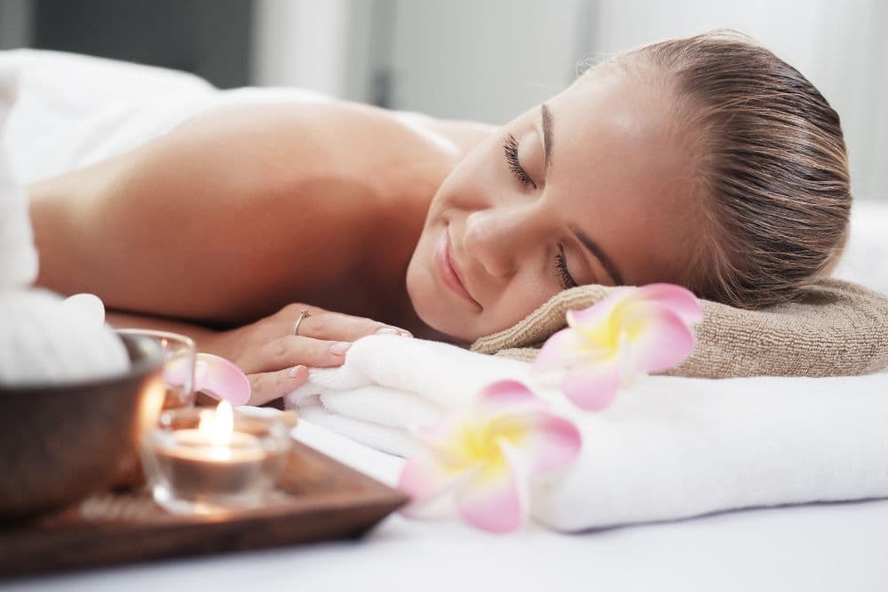 A woman relaxes on a massage table surrounded by candles and flowers.
