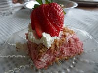 A slice of strawberry dessert topped with whipped cream and a fresh strawberry on a glass plate.