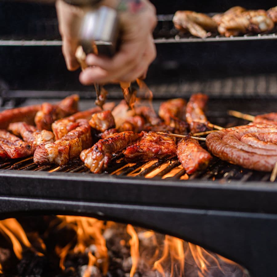 Close-up of grilled meats being tended to on a barbecue.
