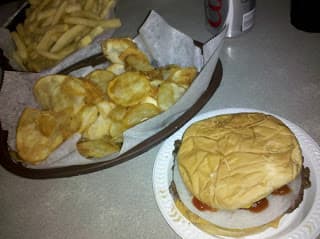 A plate with a hamburger topped with ketchup next to a serving of fries and potato chips.