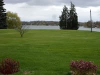 A lush green lawn with a lake and cloudy sky in the background.