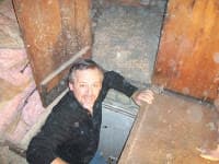 A man emerges from a dusty wooden opening, smiling as he looks up from below.