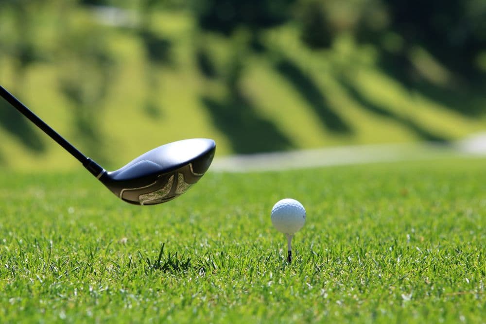 A golf club is poised above a white golf ball on a tee in a grassy field.