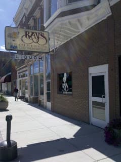 A storefront with a sign reading "Rays" and a liquor shop, featuring large windows and a pedestrian on the sidewalk.