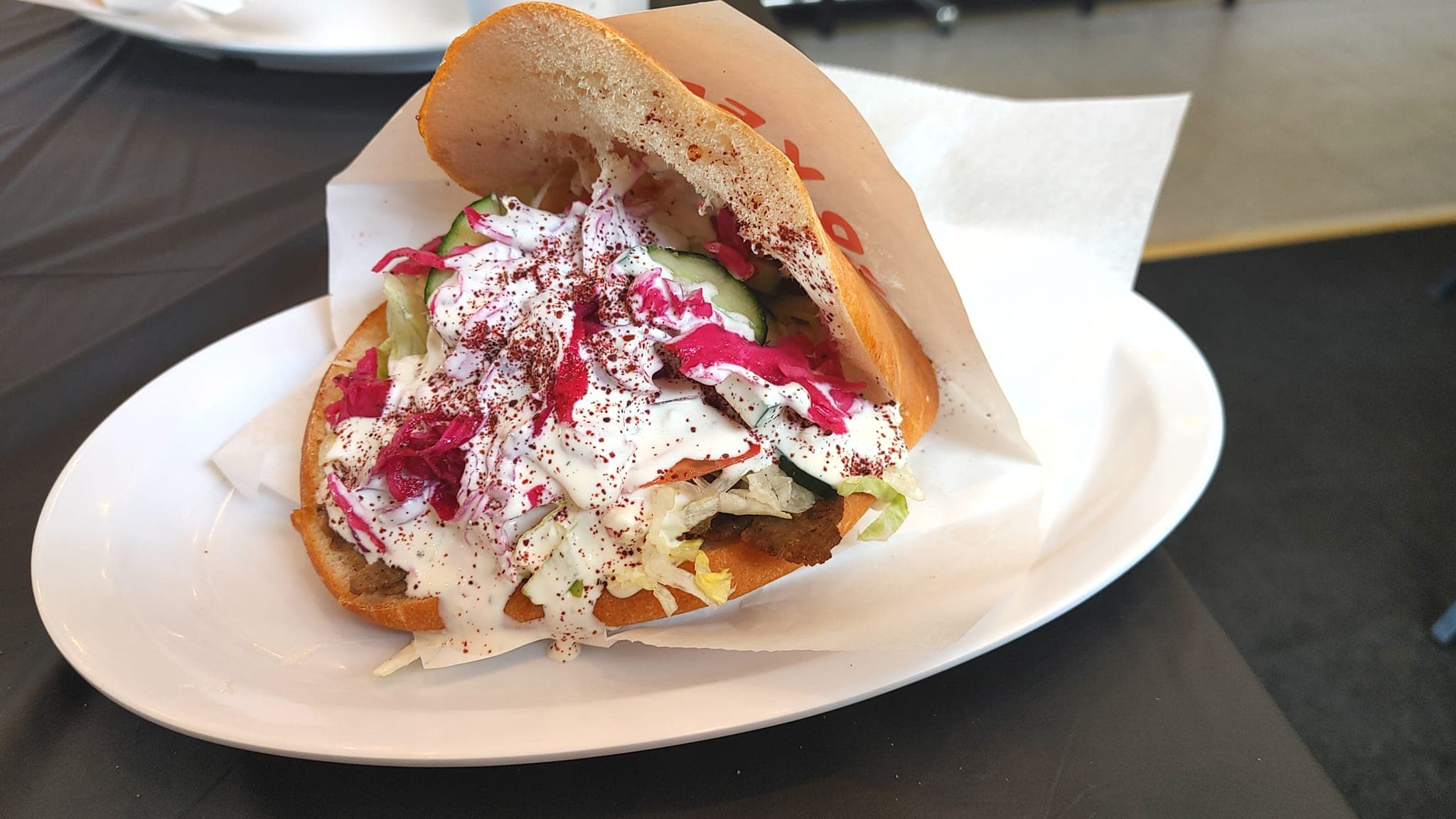 A colorful sandwich filled with vegetables and topped with white sauce and spices, served on a white plate.