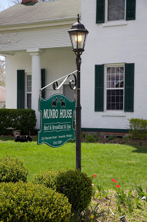 Munro House Green sign on lamp post surrounded by shrubbery in front of white business