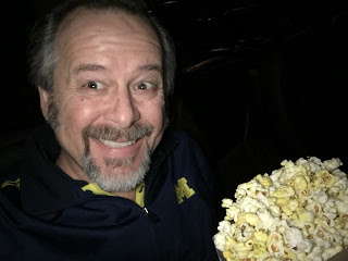 dark theater with man in blue shirt enjoying a large bag of popcorn