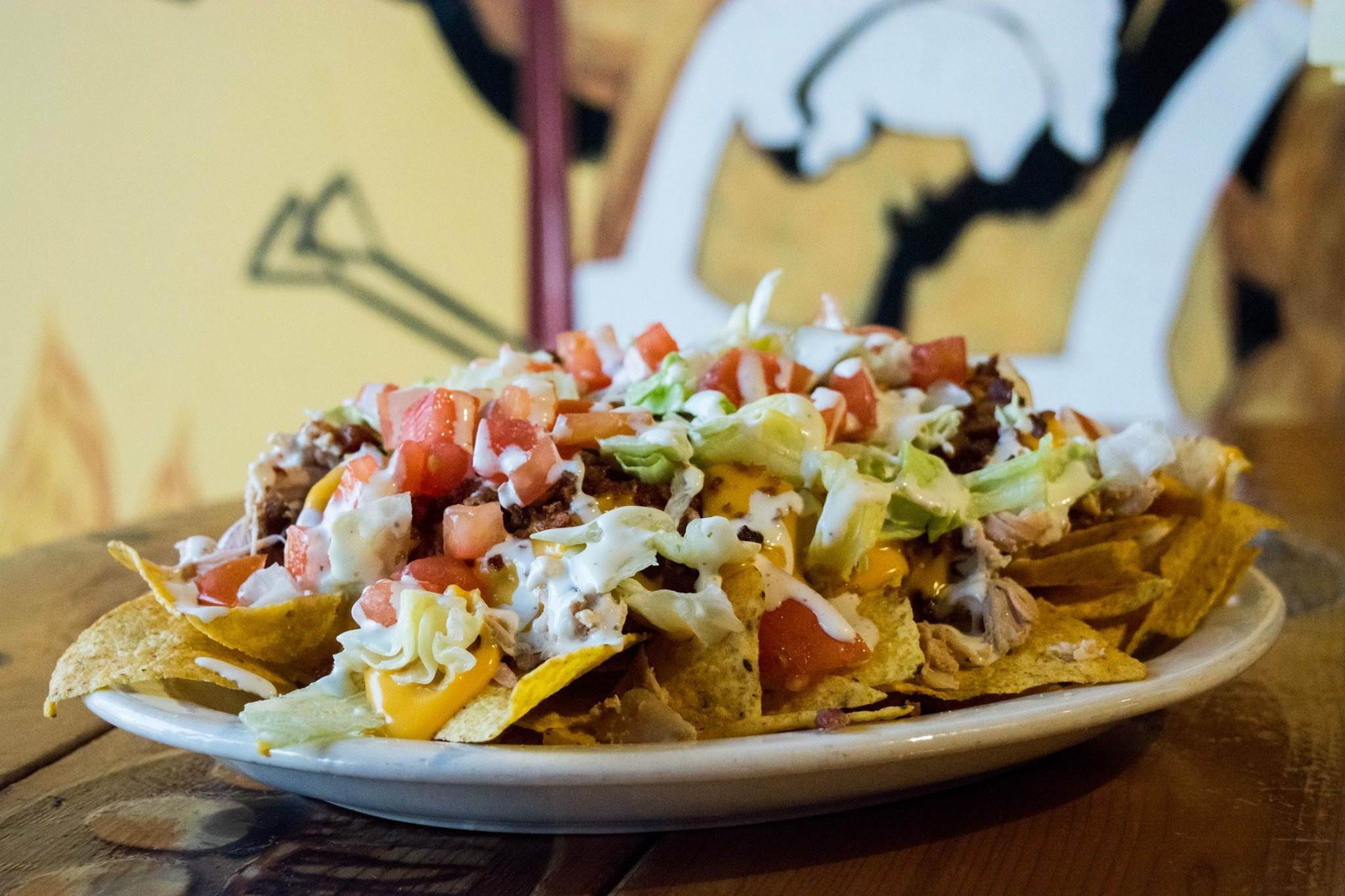 A plate of nachos with red tomatoes, cheese, lettuce, and pulled pork